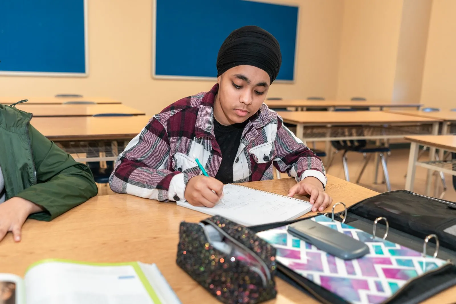 Teenage student writing at a classroom desk during a timed practice test